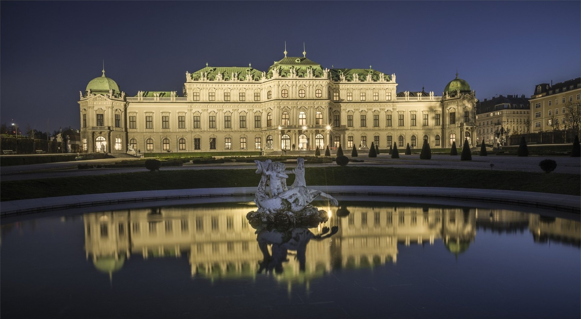 HD desktop wallpaper featuring a beautifully illuminated man-made palace at night, reflected in a calm water fountain in the foreground.