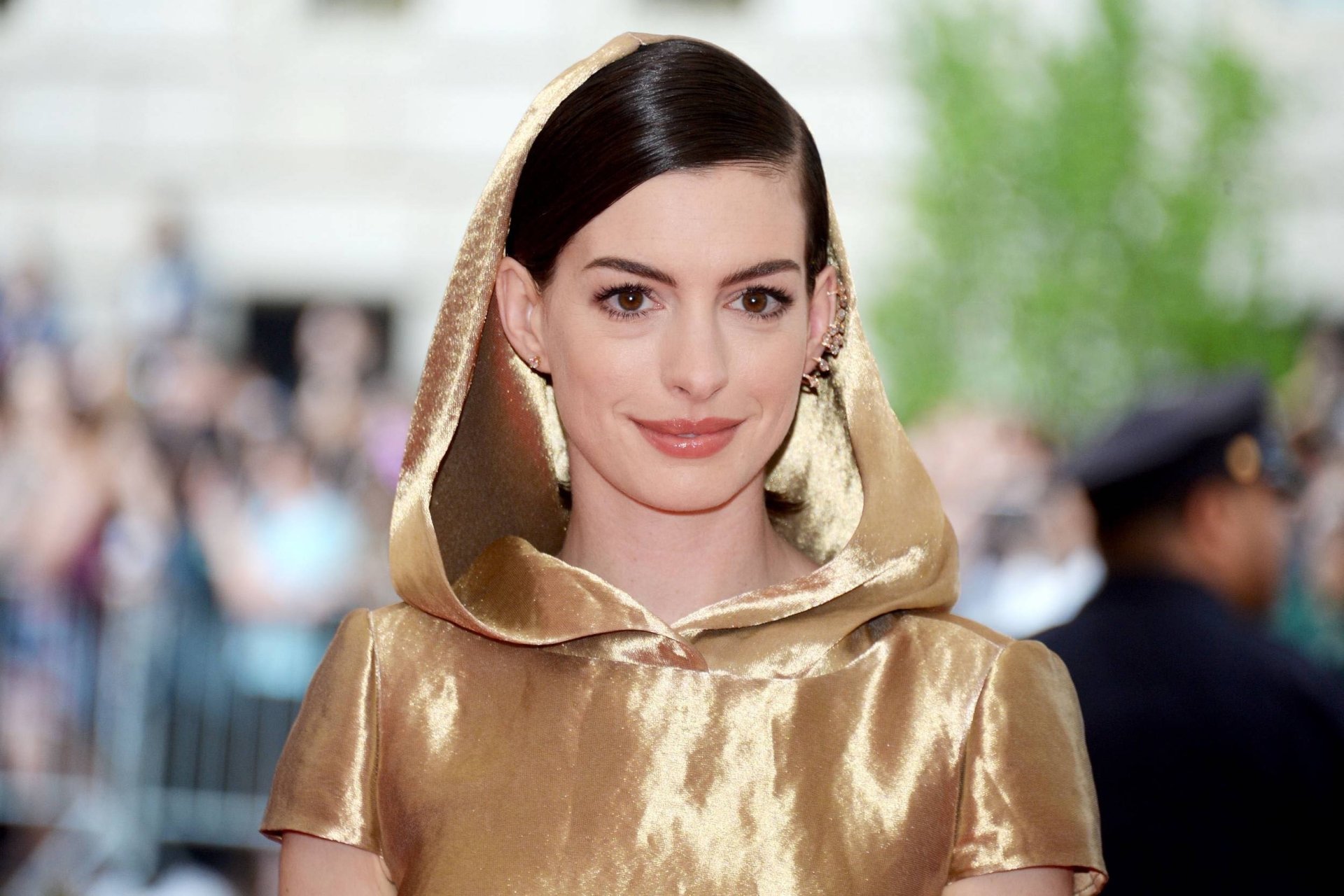 HD wallpaper of American actress Anne Hathaway with black hair, brown eyes, and a warm smile, captured with a soft depth of field background.