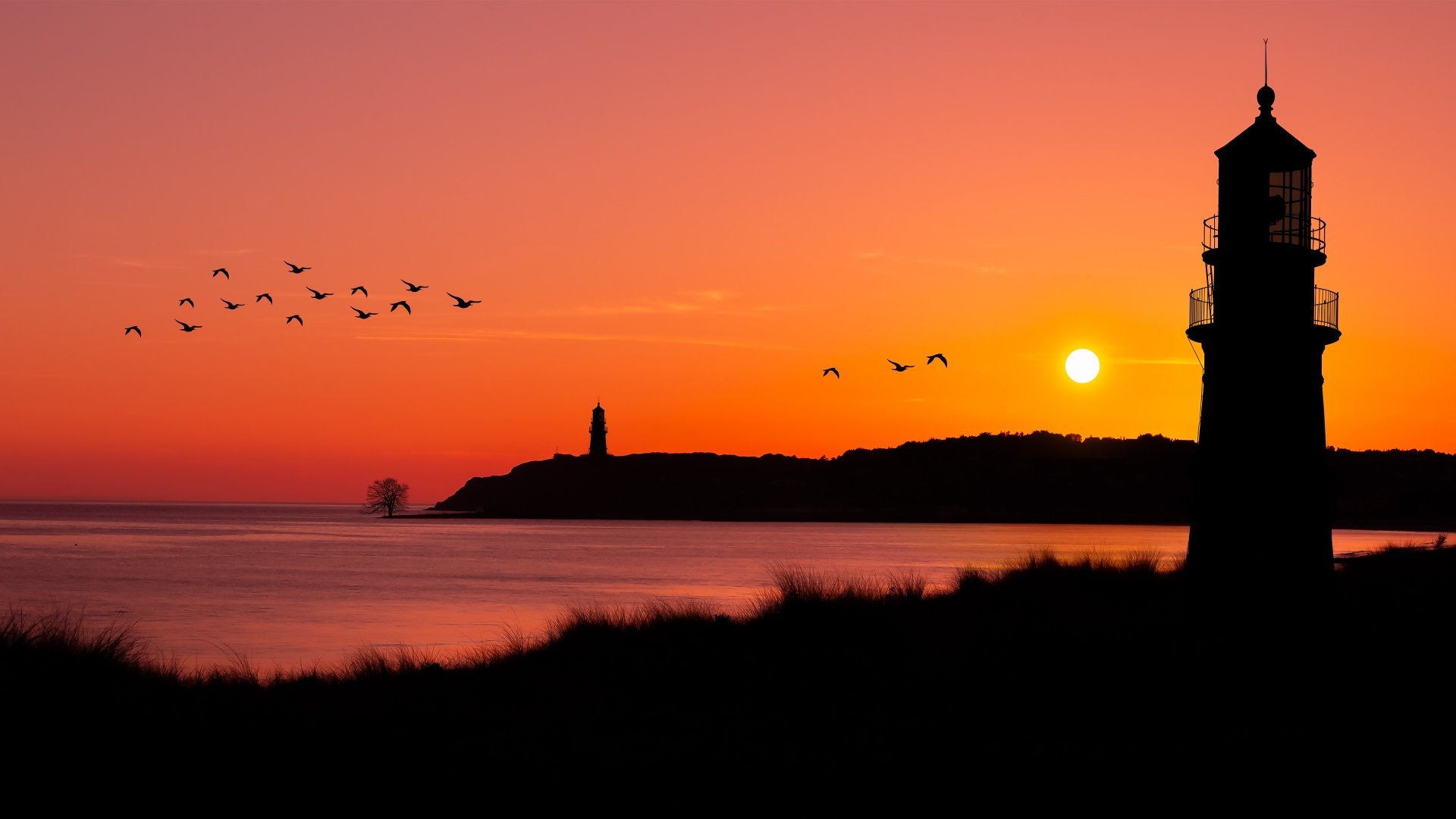 4K Ultra HD wallpaper showing a flock of birds flying over the ocean at sunset with two lighthouses silhouetted against the vibrant sky.