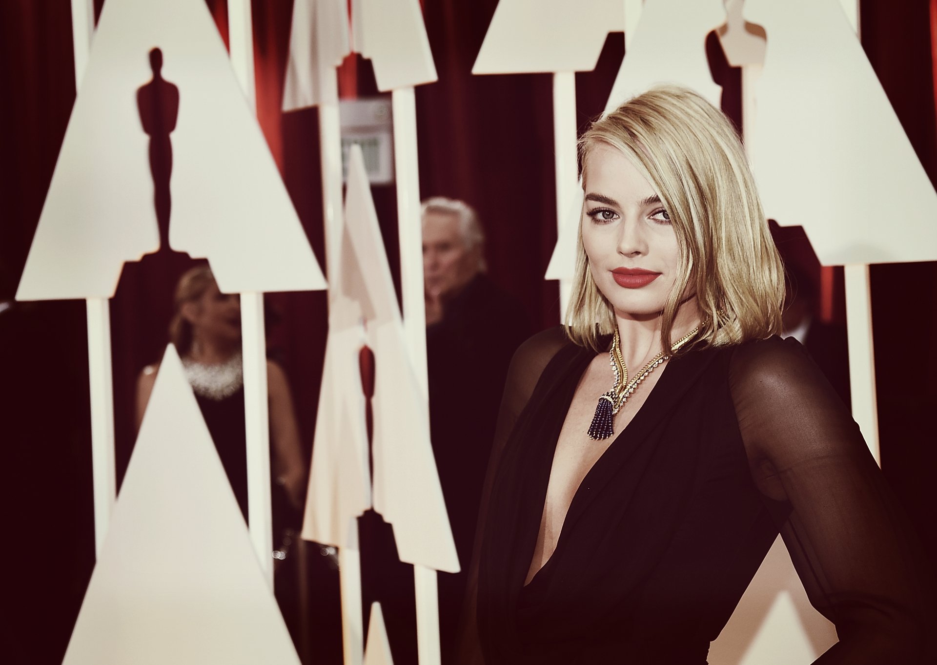 Blonde Australian actress Margot Robbie, wearing a necklace and red lipstick, poses against an elegant backdrop. HD desktop wallpaper and background.