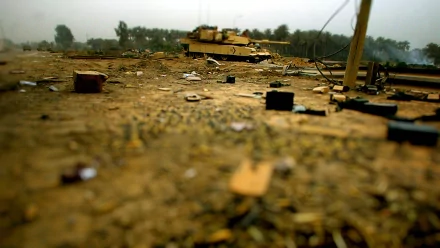 HD PC desktop wallpaper: military tank on a debris-strewn, dusty battlefield with a shallow depth of field and blurred tree line in the background.