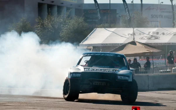 4K Ultra HD PC desktop wallpaper: rallying sports scene — a drifting rally car tearing through an urban course, smoke plumes, spectators and tents.