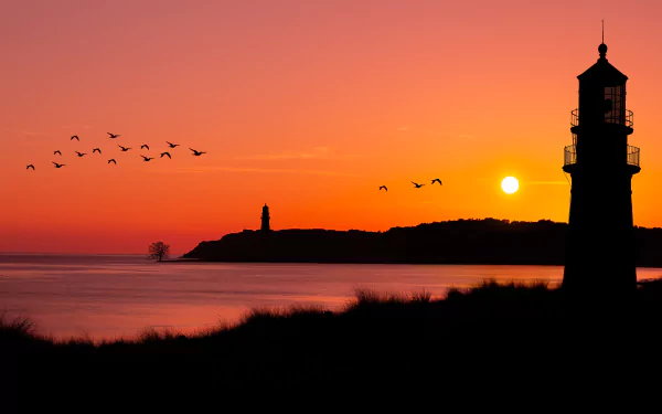 4K Ultra HD wallpaper showing a flock of birds flying over the ocean at sunset with two lighthouses silhouetted against the vibrant sky.