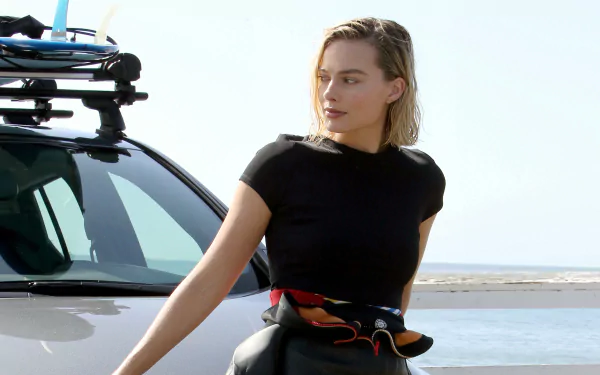 Blonde celebrity Margot Robbie in a casual black outfit leaning against a car by the beach, captured in stunning 4K Ultra HD for PC desktop wallpaper.