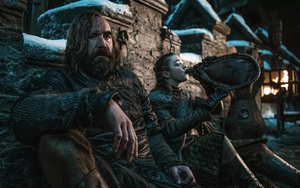 Sandor Clegane and Arya Stark from Game of Thrones sit in a snowy village, cloaked and wary by a lantern-lit hearth — 2K Quad HD PC desktop wallpaper.