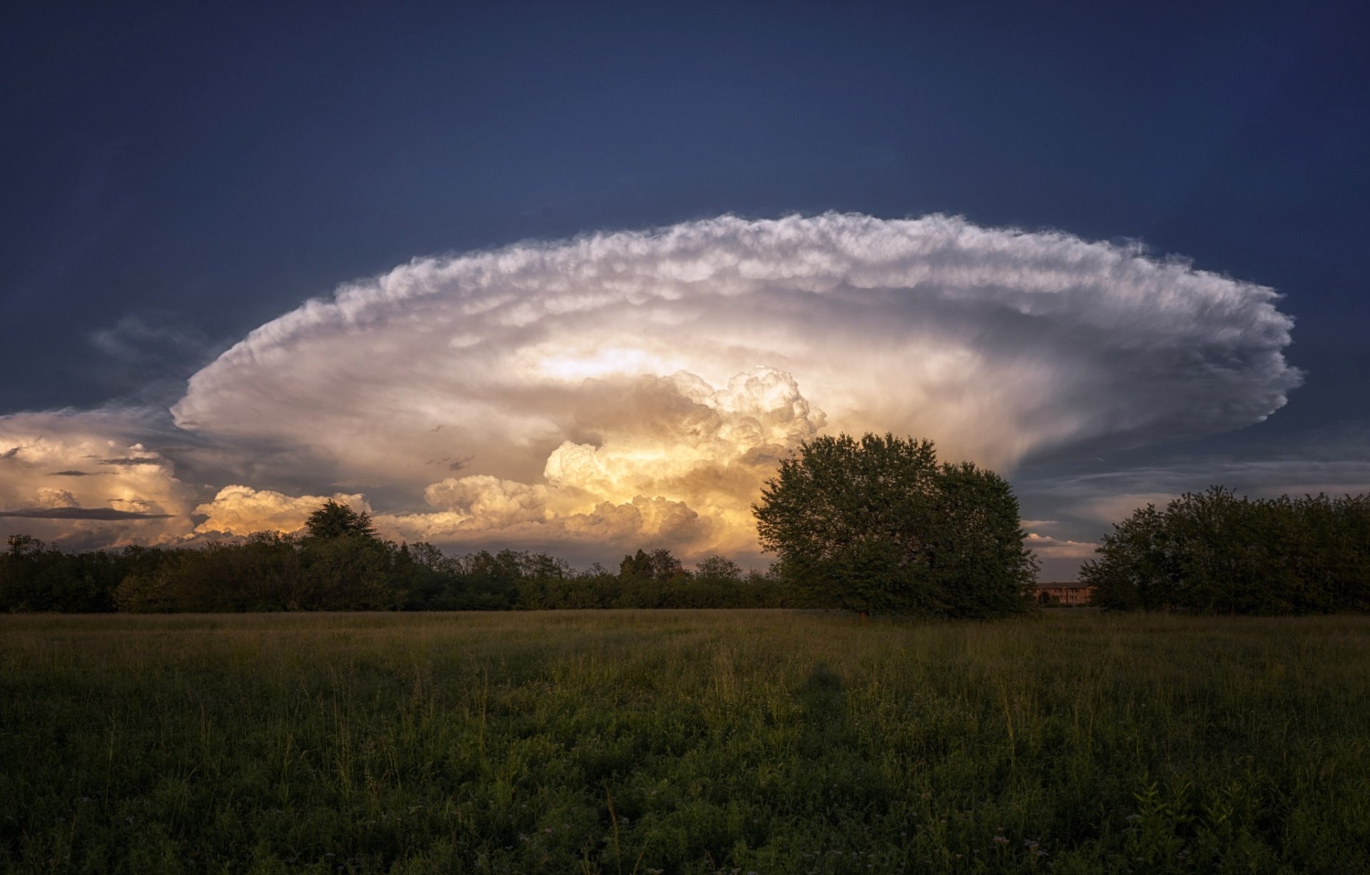 HD PC desktop wallpaper showcasing a dramatic sky with a large, illuminated cloud formation over a green field and trees at sunset.