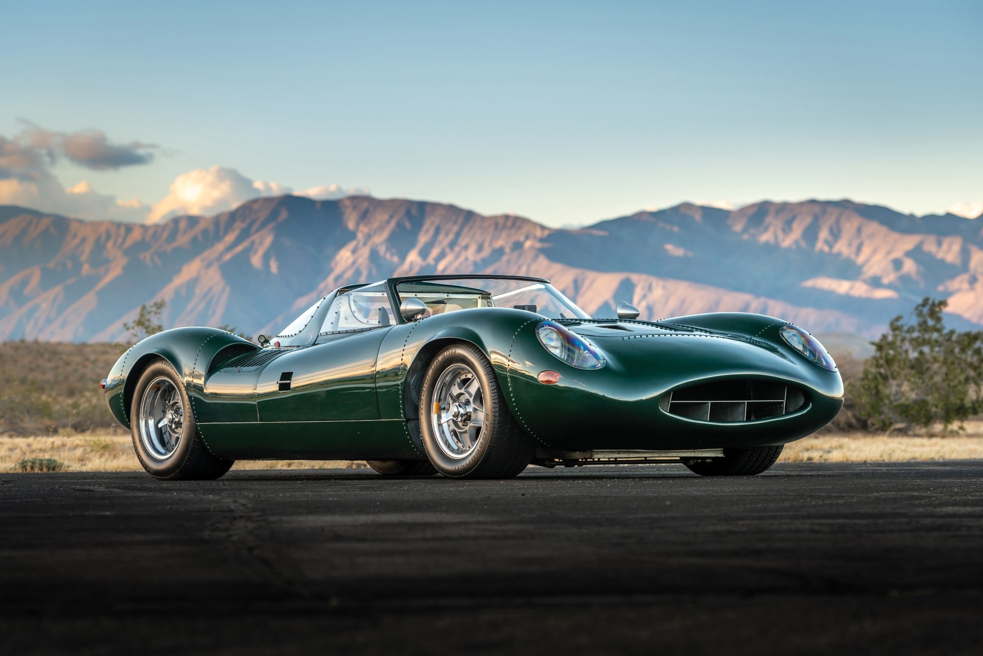 Green Jaguar XJ13 race car roadster parked on an open road with mountains in the background, shown in 4K Ultra HD PC desktop wallpaper quality.