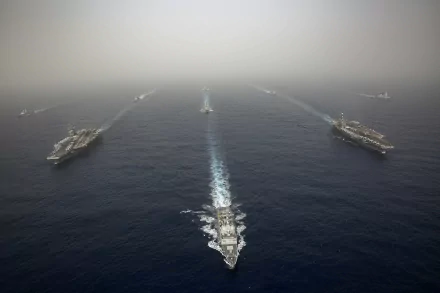 A fleet of American Navy warships, including aircraft carriers, sails across the open sea, captured in an HD military naval fleet wallpaper.