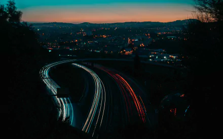 A 4K Ultra HD night cityscape featuring a winding road with light trails captured through time-lapse photography, glowing against the darkened urban skyline.