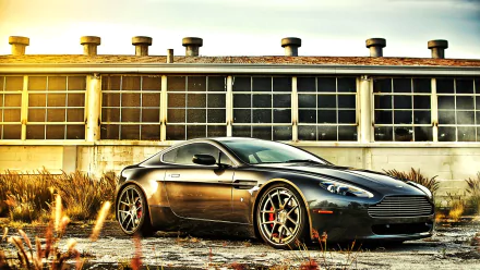 A sleek black Aston Martin DB9 grand tourer parked in front of an industrial building, showcased as a high-definition PC desktop wallpaper and background.