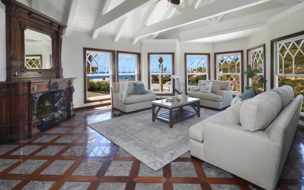 Spacious living room with man-made furniture, large windows offering ocean views, and exposed ceiling beams, captured in a 4K Ultra HD PC desktop wallpaper quality.