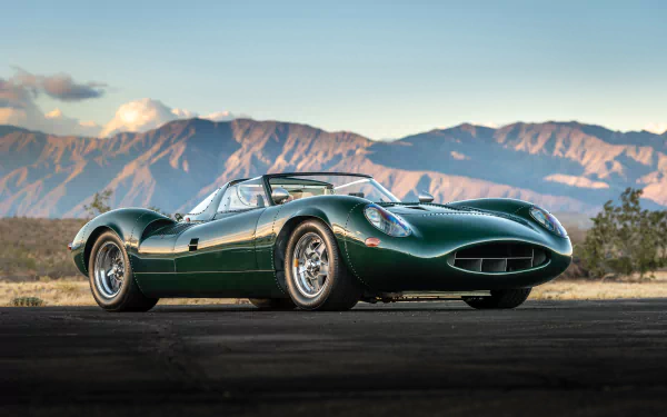 Green Jaguar XJ13 race car roadster parked on an open road with mountains in the background, shown in 4K Ultra HD PC desktop wallpaper quality.
