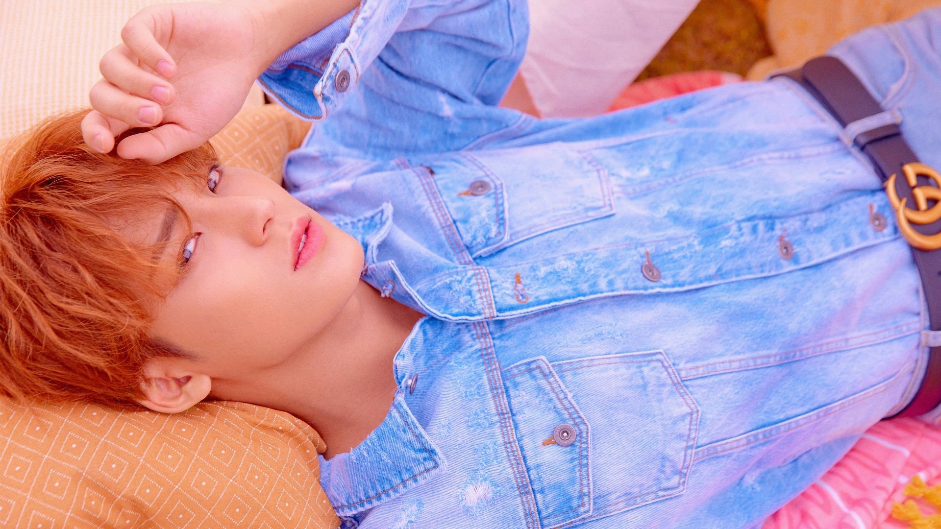 Close-up of a K-pop singer in denim reclining on a pillow, soft pastel lighting; 4K Ultra HD PC desktop wallpaper evoking Seventeen and contemporary K-pop music