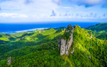 Lush forest landscape of the Cook Islands with rocky peaks and the ocean stretching under a bright blue sky, captured in vibrant HD for a desktop wallpaper.