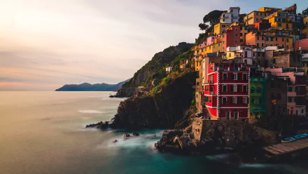 Colorful buildings of the village of Riomaggiore perched on cliffs overlooking the sea at sunset, captured in a 4K Ultra HD wallpaper featuring Manarola's coastal charm.