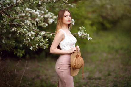 Portrait of a model woman holding a straw hat by blossoming branches, soft depth-of-field; 2K Quad HD PC desktop wallpaper