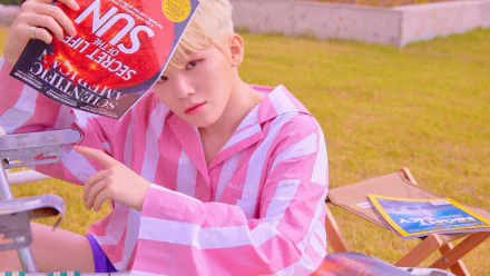 K-pop singer in a pink-and-white striped shirt lounging outdoors with a magazine, Seventeen-inspired 4K Ultra HD PC desktop wallpaper.