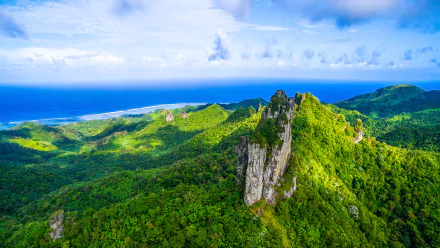 Lush forest landscape of the Cook Islands with rocky peaks and the ocean stretching under a bright blue sky, captured in vibrant HD for a desktop wallpaper.