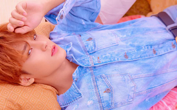 Close-up of a K-pop singer in denim reclining on a pillow, soft pastel lighting; 4K Ultra HD PC desktop wallpaper evoking Seventeen and contemporary K-pop music
