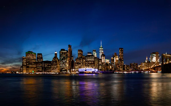 Nighttime view of Manhattan's illuminated skyscrapers and buildings in New York City, reflected on water, captured in stunning 8K Ultra HD as a vibrant urban skyline.