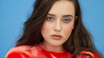 Close-up 4K Ultra HD portrait of Australian actress Katherine Langford with brunette hair and striking blue eyes against a blue background.