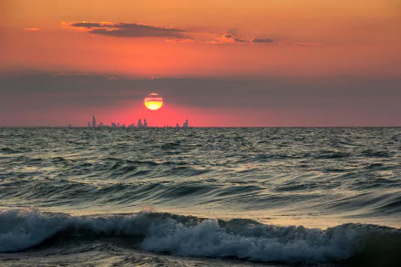 4K Ultra HD desktop wallpaper of a nature sunset over the ocean with a distant city skyline on the horizon.