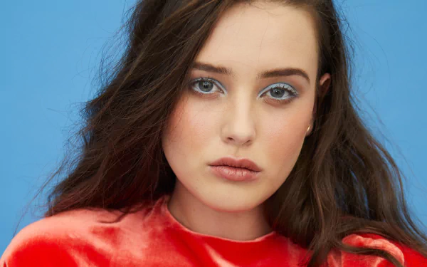 Close-up 4K Ultra HD portrait of Australian actress Katherine Langford with brunette hair and striking blue eyes against a blue background.