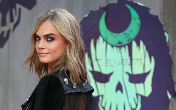 Smiling blonde English celebrity model and actress in a leather jacket, framed against a stylized skull mural, rendered as a 4K Ultra HD PC desktop wallpaper.