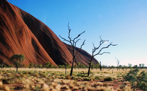 Surreal HD desktop wallpaper of Uluru in Australia, featuring a red monument rock, sparse shrubs, and a clear blue sky in a natural landscape.