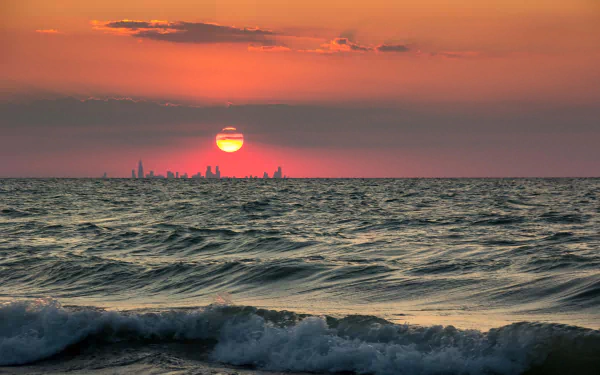 4K Ultra HD desktop wallpaper of a nature sunset over the ocean with a distant city skyline on the horizon.
