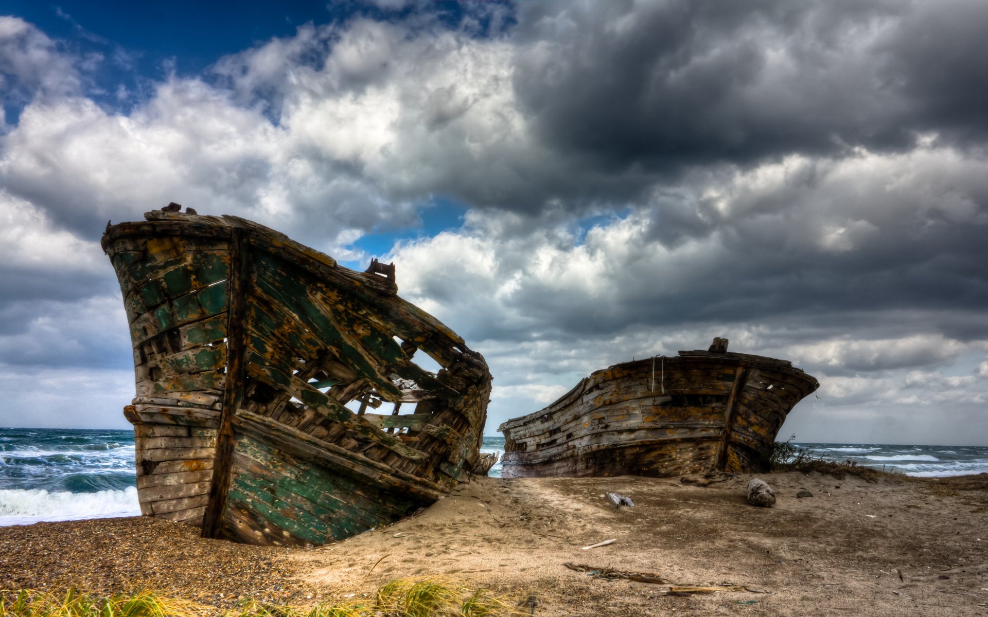 Rusting shipwrecks rest on a beach in Japan under dramatic clouds and waves, framed by an abandoned vehicle nearby in this HD desktop wallpaper.
