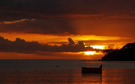 2K Quad HD PC desktop wallpaper: orange-gold sunset over ocean shoreline, clouds and sun reflected on calm water with silhouetted boat and headland.