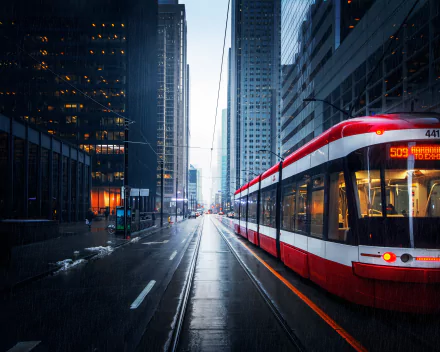 A red and white Toronto tram travels along wet city streets lined with tall glass skyscrapers under a cloudy sky, captured in 4K Ultra HD resolution.