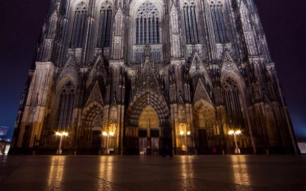 HD desktop wallpaper featuring the majestic Cologne Cathedral, showcasing its intricate Gothic architecture illuminated at night, highlighting its religious significance.