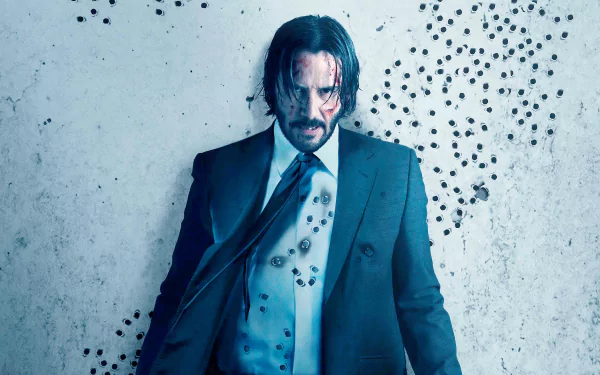 Keanu Reeves as John Wick in a dramatic 4K Ultra HD movie wallpaper from John Wick: Chapter 2, standing against a wall marked with bullet holes.