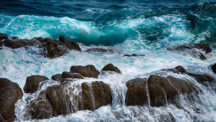 HD desktop wallpaper capturing powerful ocean waves crashing against rugged rocks, showcasing the dynamic beauty of nature and the untamed energy of the sea.