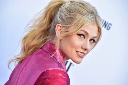 Close-up 2K Quad HD PC desktop wallpaper of a smiling blonde actress glancing over her shoulder in a pink jacket.