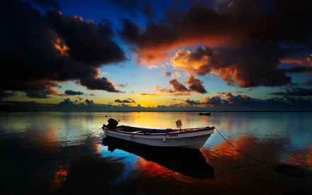 HD desktop wallpaper of a small boat floating on calm water during a vibrant sunset with dramatic clouds and colorful reflections.