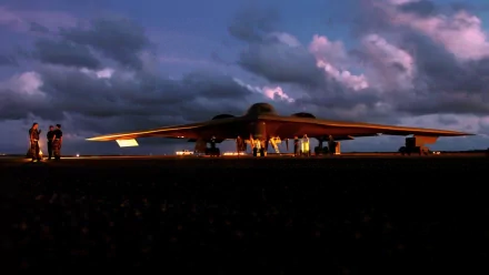 A Northrop Grumman B-2 Spirit stealth bomber is shown on the tarmac at dusk, surrounded by military personnel, creating a striking HD desktop wallpaper.