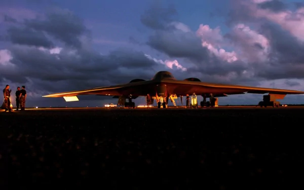A Northrop Grumman B-2 Spirit stealth bomber is shown on the tarmac at dusk, surrounded by military personnel, creating a striking HD desktop wallpaper.