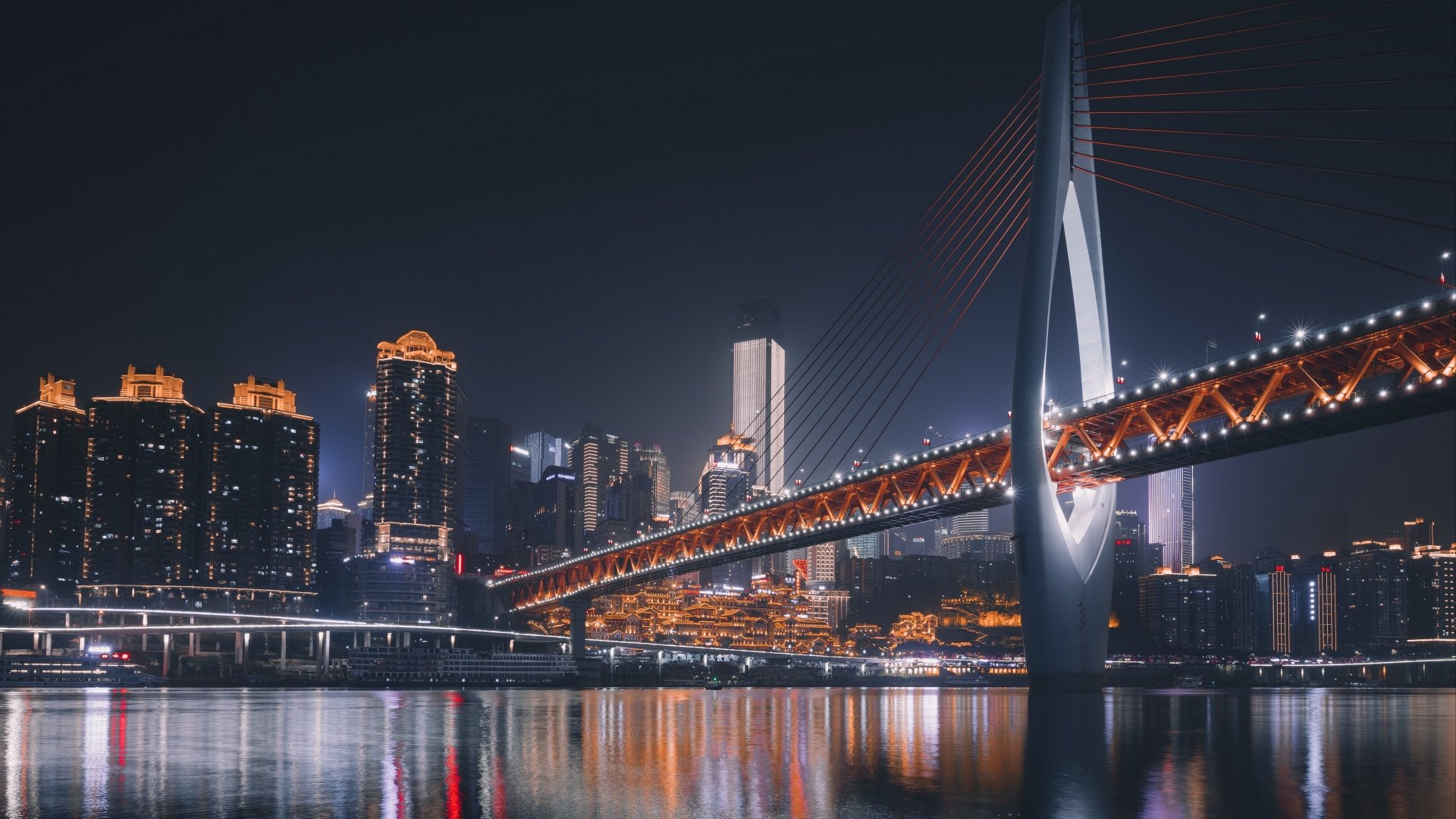 Chongqing night skyline with illuminated skyscrapers and a lit cable-stayed bridge reflected on the river, 4K Ultra HD PC desktop wallpaper of a man-made cityscape in China.