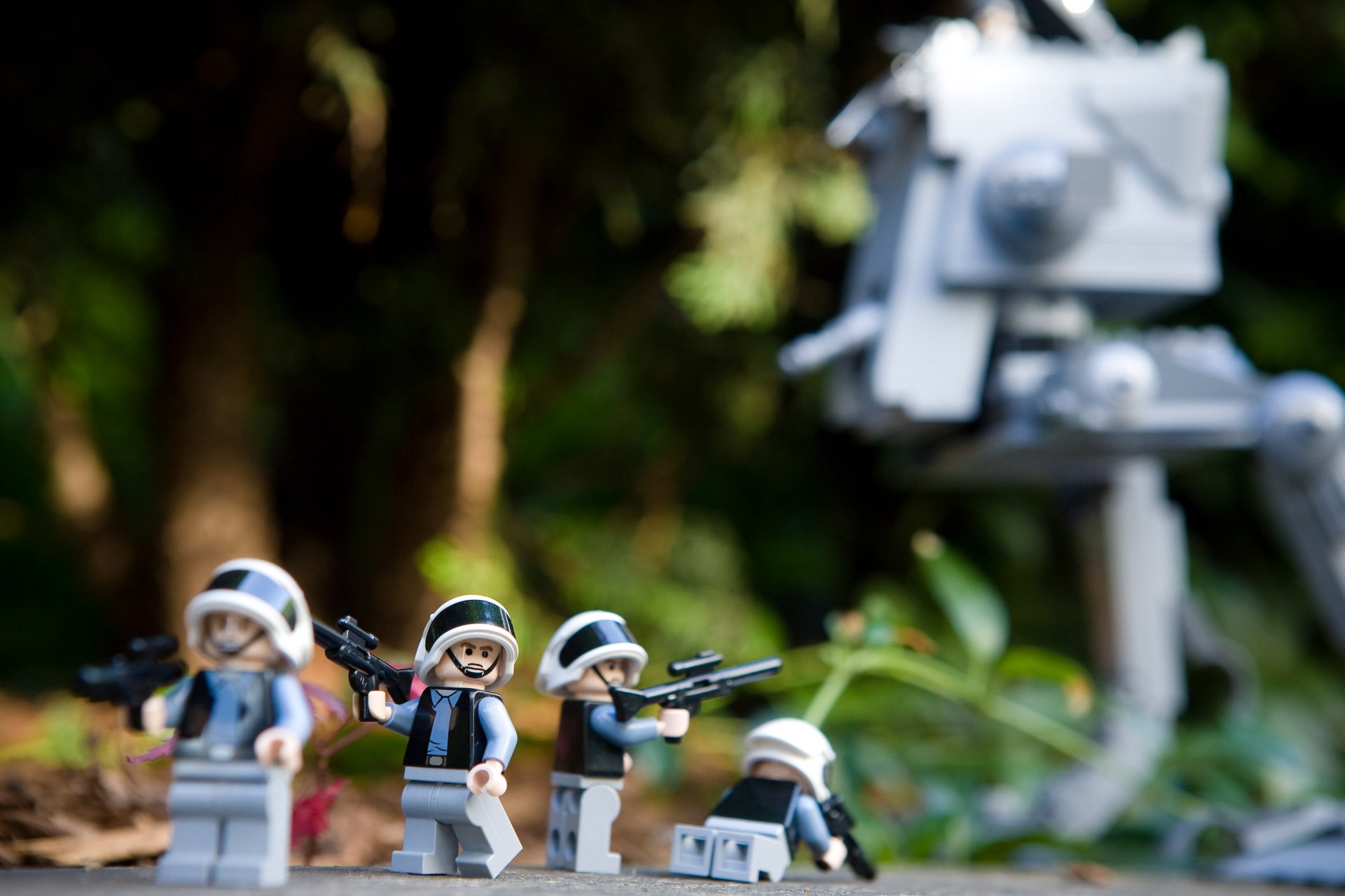 HD desktop wallpaper featuring Lego Star Wars minifigures posed in a forest setting with a blurred AT-ST walker in the background, blending sci-fi and playful themes.
