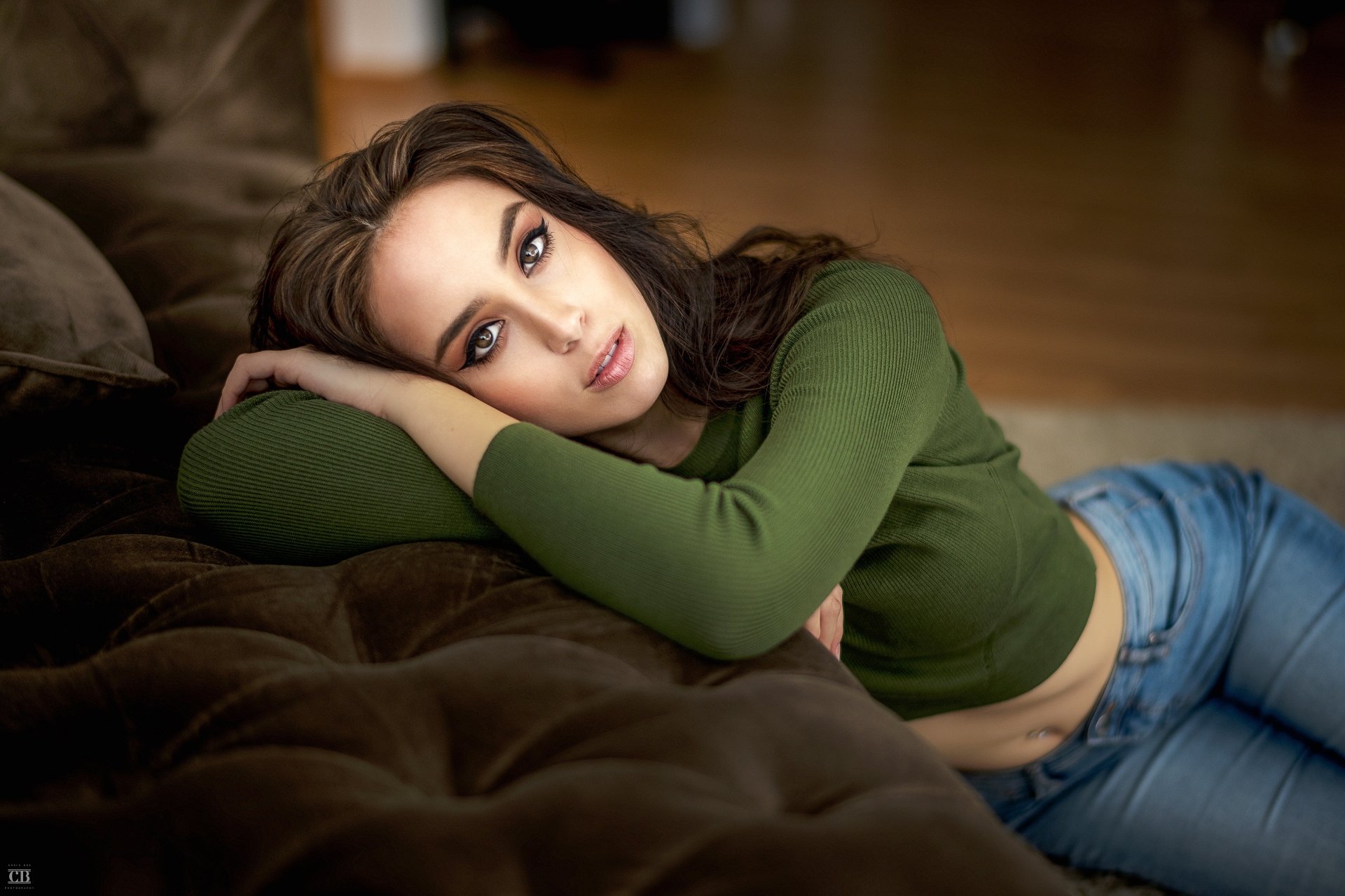 A brunette woman with brown eyes lounges on a couch, captured in a high-resolution 4K Ultra HD desktop wallpaper and background.