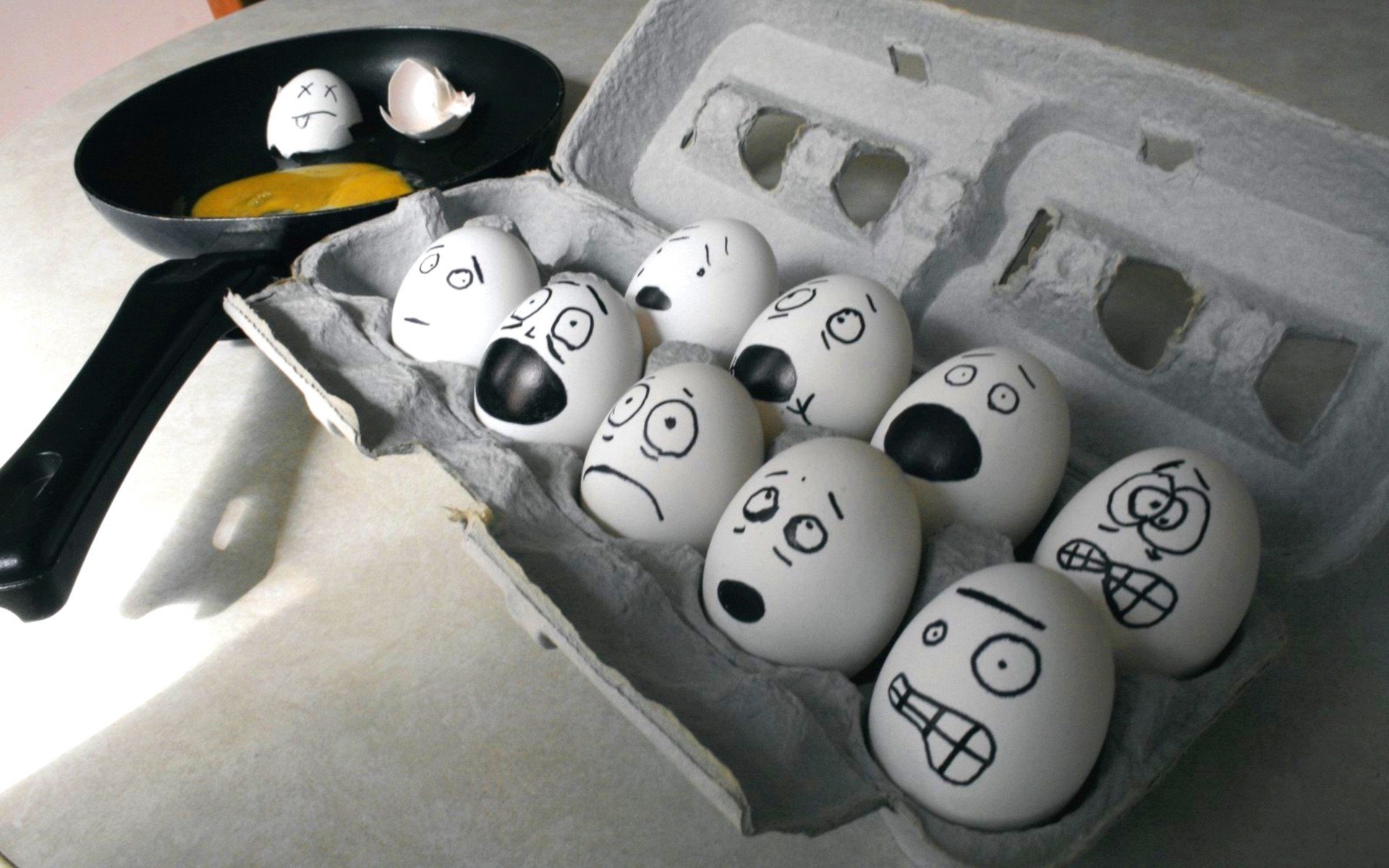 HD desktop wallpaper of eggs with various expressive faces drawn on their shells, some cracked with yolks in a pan, blending food and humor in a creative scene.