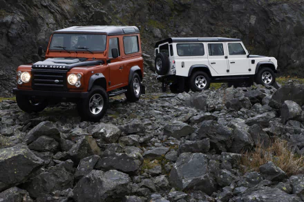 Two Land Rover Defender SUVs, one orange and one white, parked on rocky terrain captured in a 4K Ultra HD desktop wallpaper.