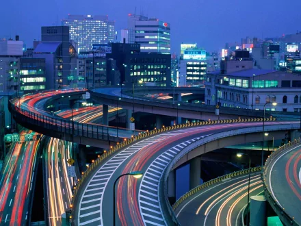 HD desktop wallpaper featuring a stunning time-lapse of Tokyo, Japan. The image showcases intertwined highways and illuminated buildings, capturing the vibrant essence of the man-made cityscape at dusk.