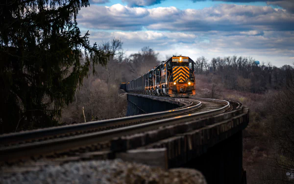 A powerful locomotive train crosses a curved railroad bridge through a wooded landscape under a cloudy sky, captured in 4K Ultra HD for a vivid PC desktop wallpaper.