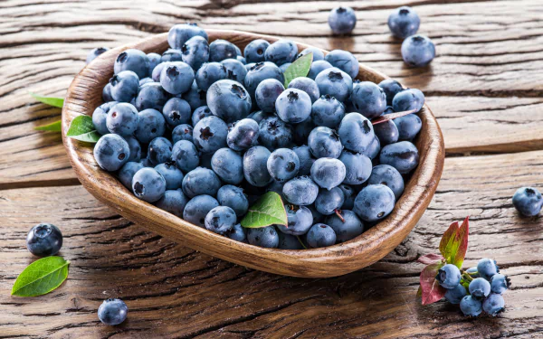 8K Ultra HD PC desktop wallpaper: still life of ripe blueberries and a few green leaves in a wooden bowl on rustic wood — fruit/berry food background.