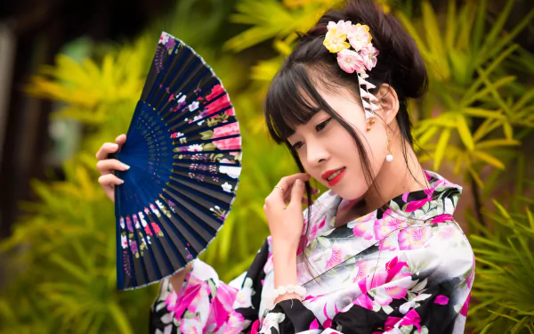 Elegant Asian woman with black hair and lipstick wears a floral kimono, holding a decorative fan amidst lush greenery in this 4K Ultra HD desktop wallpaper.