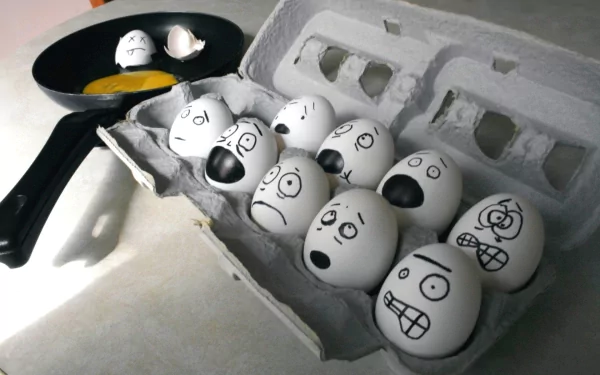 HD desktop wallpaper of eggs with various expressive faces drawn on their shells, some cracked with yolks in a pan, blending food and humor in a creative scene.